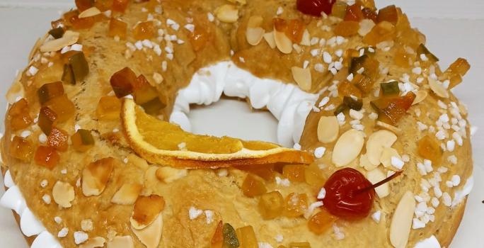 Foto da receita de Rosca de Reis. Observa-se uma rosca recheada com chantilly e decorada com frutas secas, cereja e amêndoas laminadas.