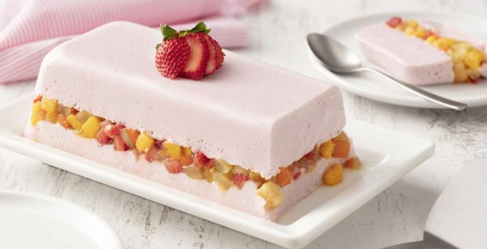 fundo de madeira branca com paninho rosa claro, um prato branco com uma camada de gelatina com iogurte de morango, uma camada de salada de frutas e mais uma camada de gelatina com iogurte de morango.