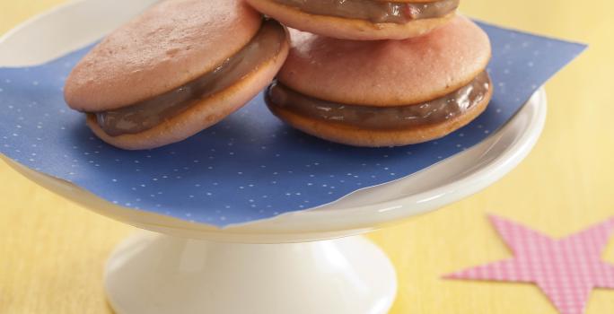 foto em tons de bege, marrom e azul de uma bancada bege vista de frente, contém um suporte para servir sobremesas com um pano azul que contém 3 biscoitos recheados com chocolate