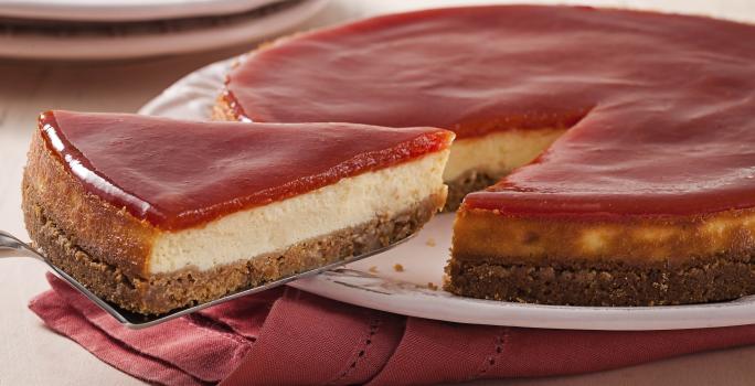 Fotografia em tons de branco e rosa de uma bancada branca com um paninho rosa, sobre ele um prato branco com torta de goiabada. Ao fundo dois pratos brancos.