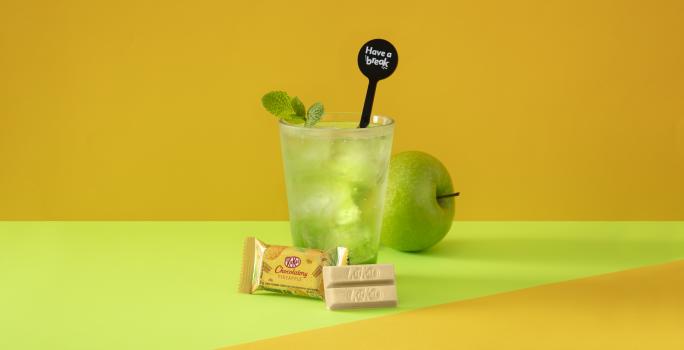 Foto da receita de Soda Italiana Apple Green. Observa-se um fundo amarelado e verde com um copo alto no centro, decorado com folha de hortelã. Uma maçã verde atrás do copo decora a foto.