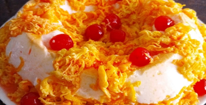 Foto em tons de amarelo da receita de pudim de clara de panetone com fio de ovos com cerejas por cima para decorar