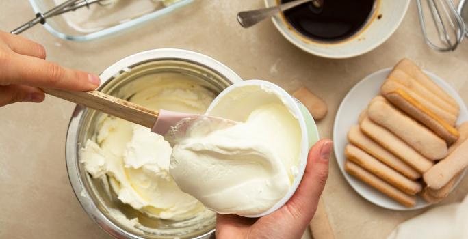 Foto da receita de Creme 4 Leites. Observa-se uma pessoa mexendo o creme dentro de uma vasilha branca.