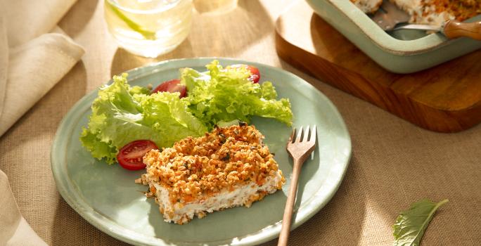 Foto da receita de quibe de abóbora de aveia servida com salada de alface e tomate sobre um pratinho azul com um garfo de madeira ao lado e ao fundo há uma forma com o restante do quibe