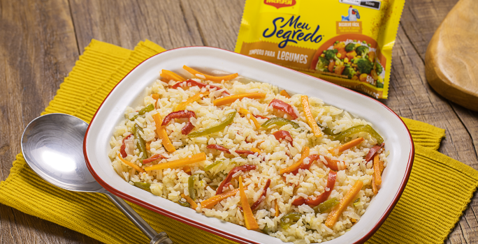 Fotografia mostra uma travessa com arroz com pimentões coloridos e uma colher servindo arroz.