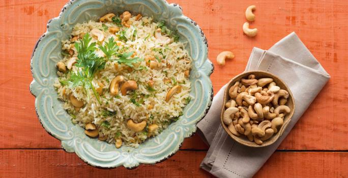 em uma mesa na cor vermelha, contém dois recipientes. Um contém o arroz e o outro as castanhas-de-caju.