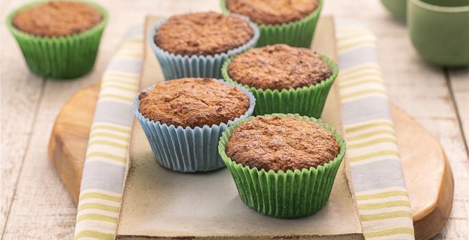 Foto da Receita de Cupcake Leve FiberMais. Observa-se uma tábua de madeira sobre um guardanapo listrado e os cupcakes em cima em forminhas verdes e azuis.