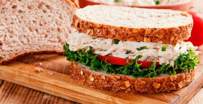 Foto da receita de Sanduíche de Salpicão de Frango. Observa-se um sanduíche bem perto expondo o recheio de frango cremoso com a salada de alface e tomate embaixo.