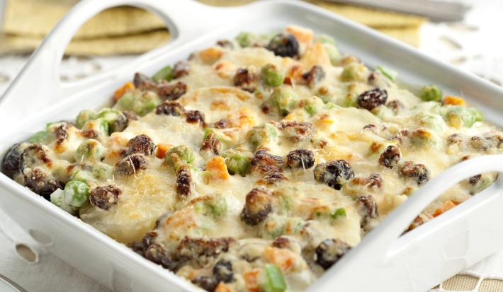 em um recipiente quadrado e branco contém batatas gratinas com uvas-passas, cenoura e pimentão