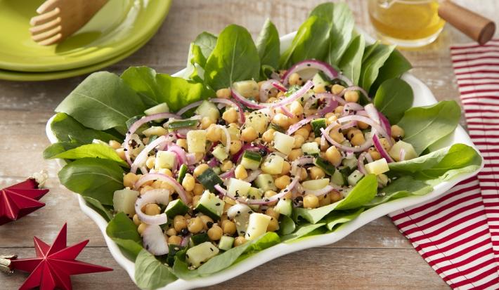 Foto em tons vivos da receita de salada de grão de bico e batata doce servida em um prato grande retangular de porcelana branca sobre uma mesa de madeira com um paninho listrado vermelho ao lado