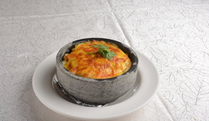 Em cima de uma mesa, prato de porcelana cinza com queijo gratinado, decorado com folha de salsa.