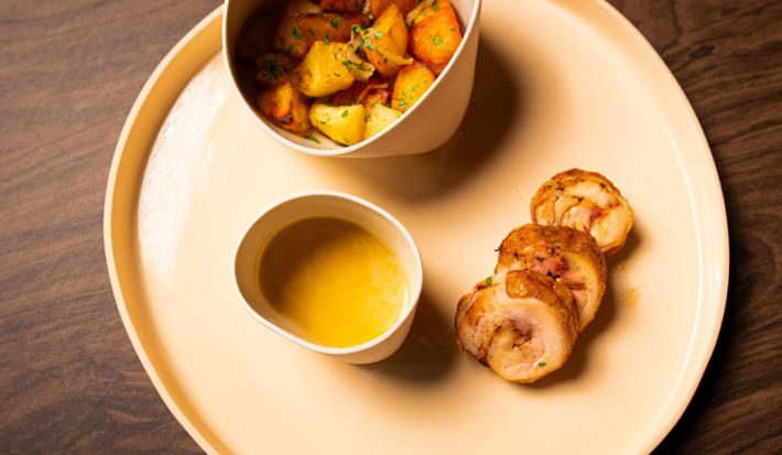 Foto da receita de BALOTINE DE FRANGO COM BATATAS LYONESE. Observa-se um prato visto de cima com o frango cortado em rodelas, servido com um molho ao lado e as batatas coradas.