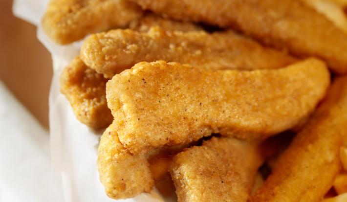 Fotografia em tons de amarelo e branco de uma cesta com um pano branco e tiras de frango dentro