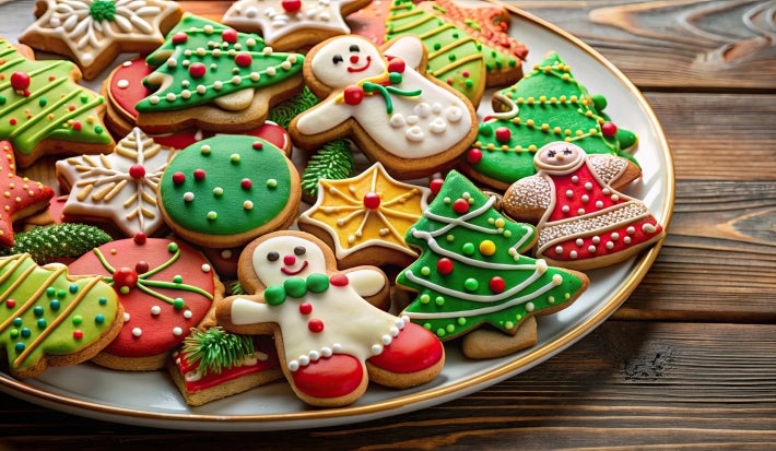 Em cima de uma mesa, prato com biscoitos em formato de árvores de Natal, bonecos de neve e biscoito redondos, decorados com glacê colorido e confeitos coloridos de bolinhas verde e vermelho.