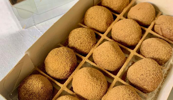Fotografia em tons de branco um várias trufas de chocolate ao centro. Todas as trufas estão polvilhadas com cacau em pó e posicionadas dentro de uma forma da papel