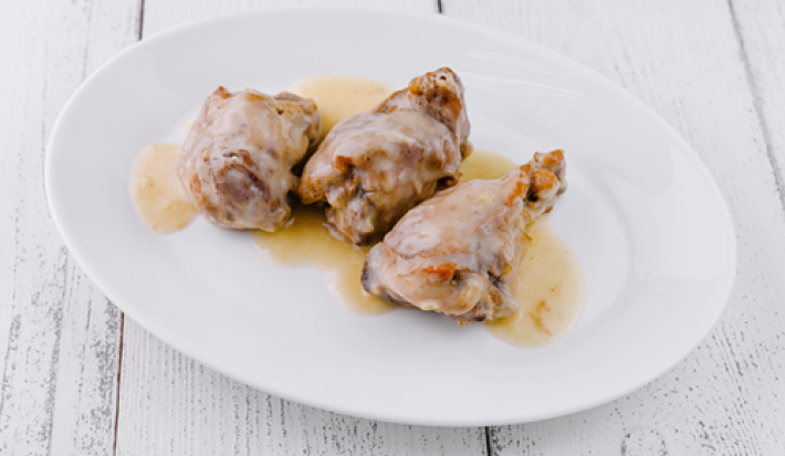 A imagem mostra cortes de frango assado com molho de vinho sobre um prato branco
