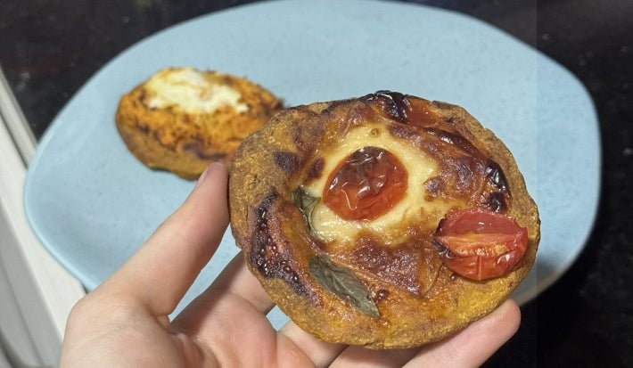 Fotografia de uma mão segurando uma mini pizza com massa de abóbora. No funo tem um prato raso azul com outra mini pizza.
