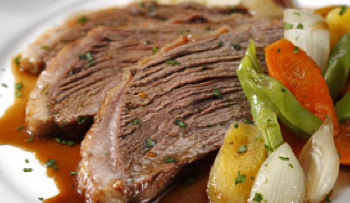 Fotografia em tons de marrom em uma mesa com um pano laranja e um prato raso branco em cima com duas fatias de picanha e os legumes.