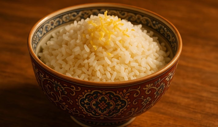 Em cima de uma mesa, tigela redonda branca com porção de arroz, decorado com raspas de limão.