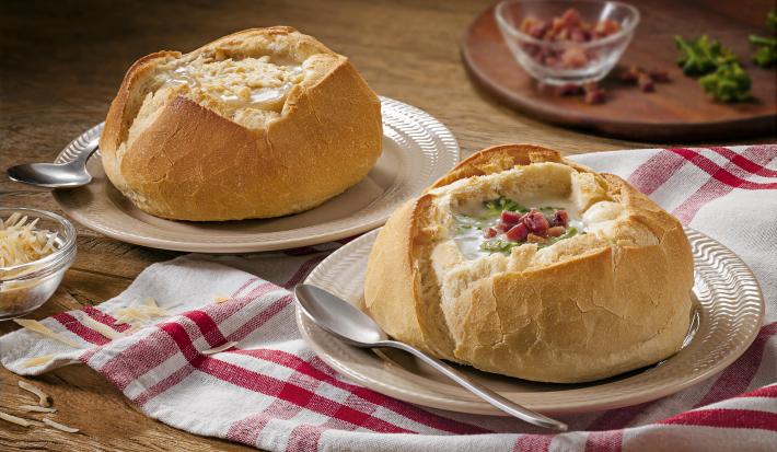 Foto de um pão italiano com sopa creme de queijo dentro e bacon decorando em cima da receita