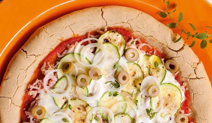 em um prato redondo laranja contém uma pizza com abobrinha, peito de peru e requeijão.