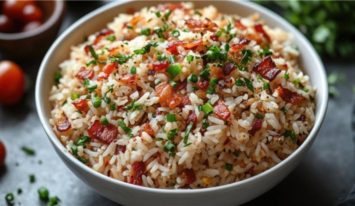 Em cima de uma mesa, tigela branca com arroz soltinho, bacon picado em pedaços, decorado com salsinha picada.