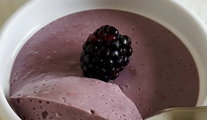 Fotografia em tons claros de três ramekins brancos sobre uma mesa branca. Dentro dos ramekins têm mousse de amora, com uma amora decorando cada um.