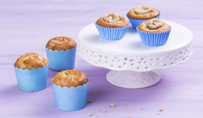 Foto de 6 cupcakes em forminhas azuis. 3 destes estão em uma mesinha branca e 3 estão ao lado da mesinha