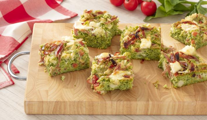 Fotografia em tons de verde e vermelho, ao centro uma tábua de madeira com 6 fatias da torta de espinafre, ao fundo um pano quadriculado vermelho e branco.