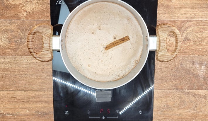 Leite com chocolate e canela cozinhando na panela sobre fogão portátil preto.
