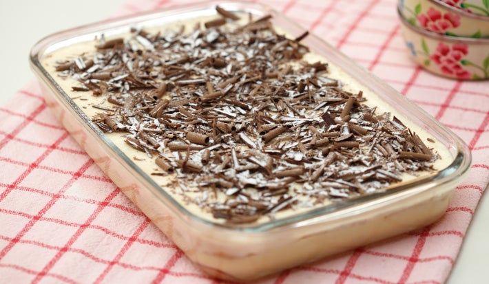 Imagem de uma travessa com o pavê coberto com raspas de chocolate sobre uma toalha quadriculada vermelha.