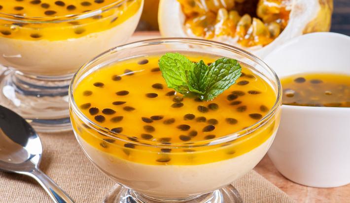 Foto da receita de Mousse de Maracujá Zero Lactose. Observa-se dois potinhos de vidro transparentes com a mousse de maracujá em cima, decoradas com as sementes da fruta.