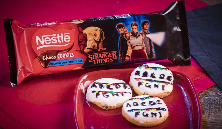 Cookies redondos cobertos com chocolate branco, decorados com luzinhas coloridas e letras feitas em chocolate escuro, lembrando um varal iluminado.