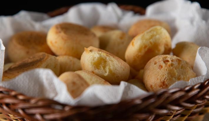 Várias unidades de pães de queijo colocadas dentro de um cesto sobre uma toalha branca.