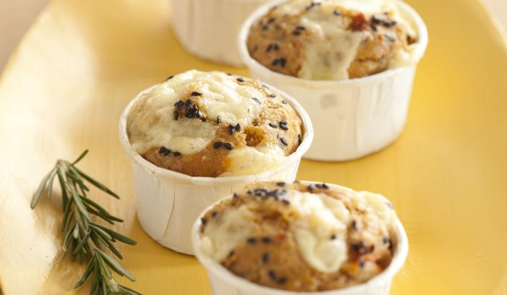 Fotografia em tons de amarelo em uma bancada de madeira clara, um prato amarelo retangular com forminhas brancas grandes com os muffins salgados dentro delas.