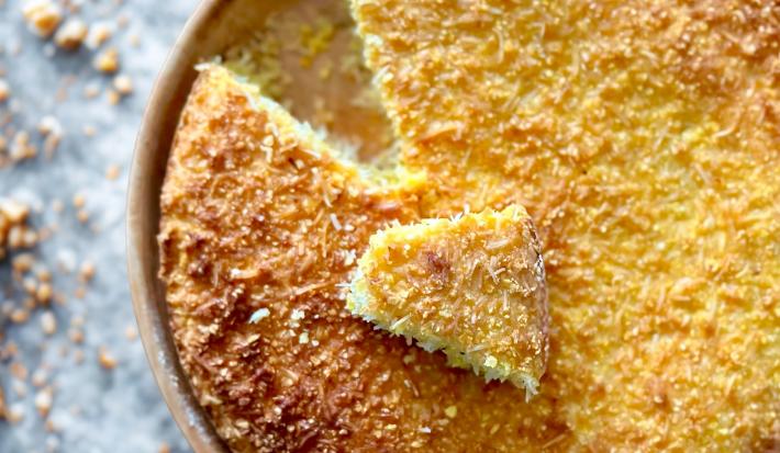 Fotografia mostra bolo de milho dourado, pedacinhos de coco visíveis na superfície.
