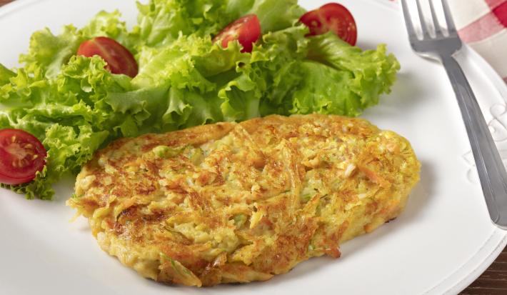 Fotografia em tons de branco, verde e amarelo de um prato branco redondo com folhas de alface com tomate, uma tortilha e um garfo sobre o prato. Ao fundo um paninho xadrez vermelho e branco.