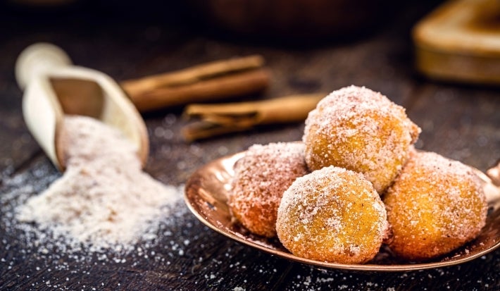 Em cima de uma mesa, prato com bolinhos de chuva, polvilhado com açúcar de confeiteiro.