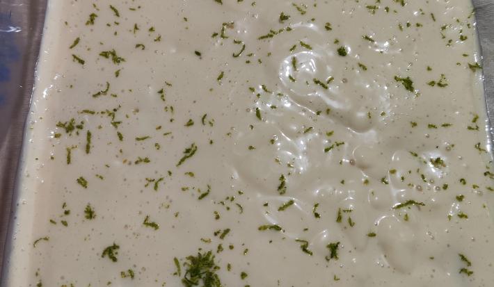 Fotografia vista de cima de um recipiente refratário de vidro com uma sobremesa de mousse de limão com raspas de limão e tostines especiarias.