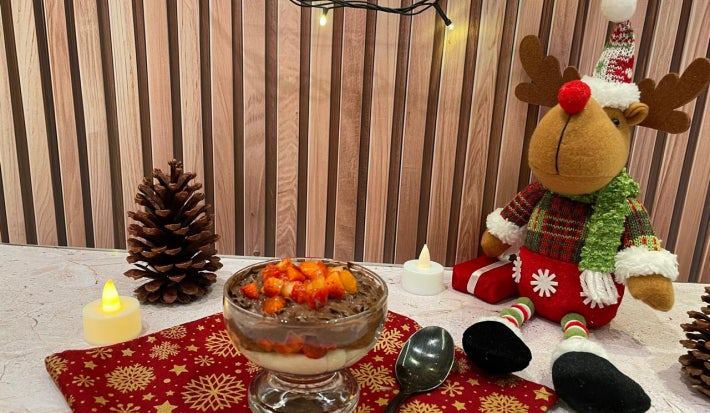 Fotografia em tons de vermelho e natal com uma taça de vidro e pavê de chocolate e morango ao centro.