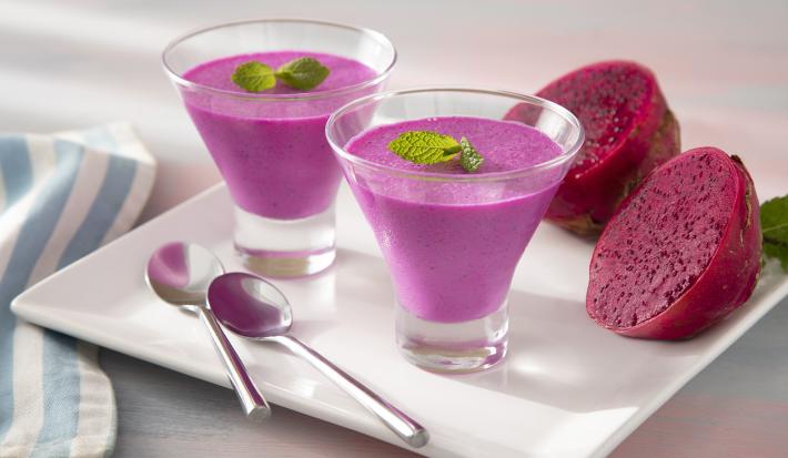 Foto da receita de Mousse de Pitaya e Leite Moça. Observa-se duas taças de vidro com a mousse cor-de-rosa decorada com hortelã em cima de um prato branco quadrado.