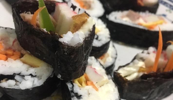 Fotografia de fatias grossas de gimbap brasileiro com arroz, cenoura, kani e pepino sobre um prato branco.