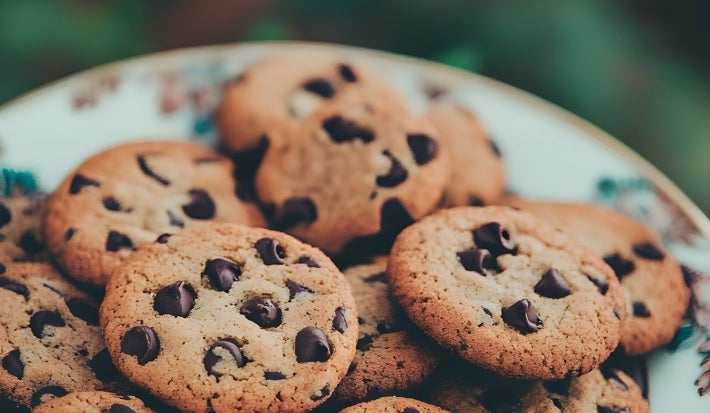 Em cima de uma mesa, prato redondo com biscoitos crocantes com gotas de chocolate.