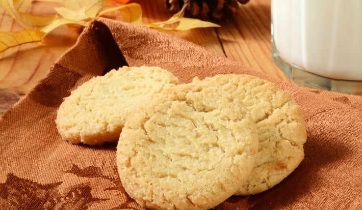 Em cima de uma mesa, pano de prato marrom com biscoitos redondos crocantes e dourados.