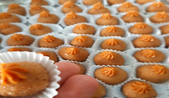 Foto em tons de laranja da receita de brigadeiro de churros servida em várias porções, com destaque para uma unidade sobre os dedos de uma pessoa a frente