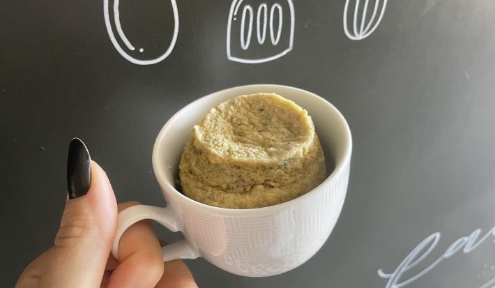 Imagem da Receita de Bolo de Caneca de Banana sem Açúcar, em uma caneca branca e ao fundo uma lousa