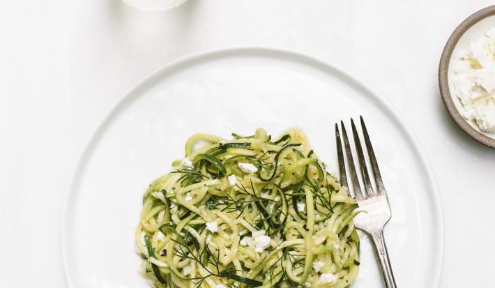 Fotografia em tons claros vista de cima de um macarrão com molho de sálvia, manteiga e vinho, com um garfo ao lado, dentro de um prato branco raso. Ao redor, outro prato com a mesma massa, e, um recipiente pequeno e fundo com molho branco cremoso.