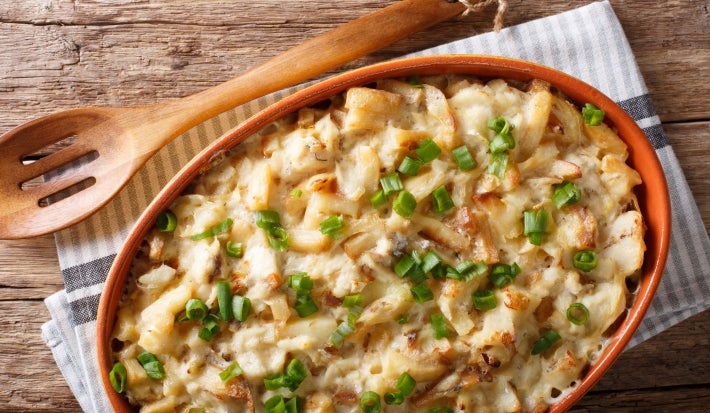 Em cima de uma mesa, recipiente com bacalhau e queijo gratinado, decorado com cebolinha picada.