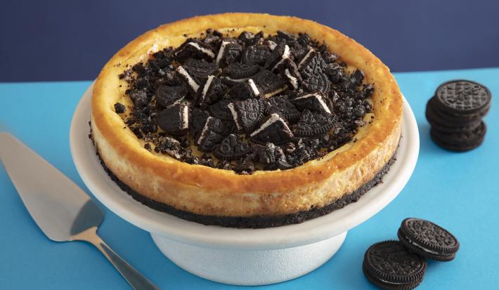 Foto da receita de Cheesecake de negresco. Observa-se a torta em uma bailarina branca com pedaços de negresco cortados no topo, em um fundo com dois tons de azuis - um mais claro e outro mais escuro.