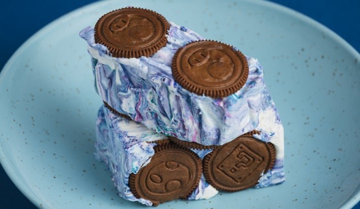 Cubos de sobremesa com creme marmorizado azul e branco e biscoitos de chocolate, servidos em prato azul.